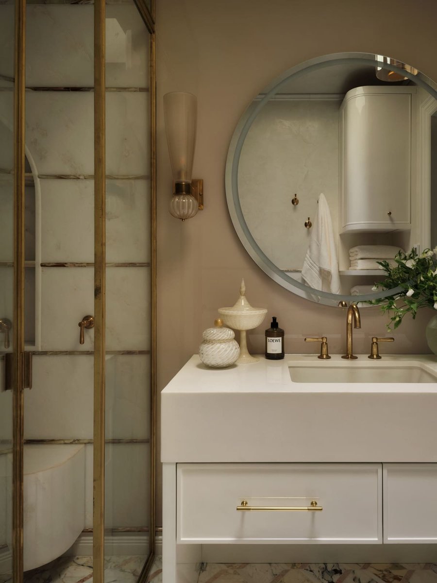 Elegant bathroom vanity with round mirror, brass fixtures, and glass shower, located in Toronto