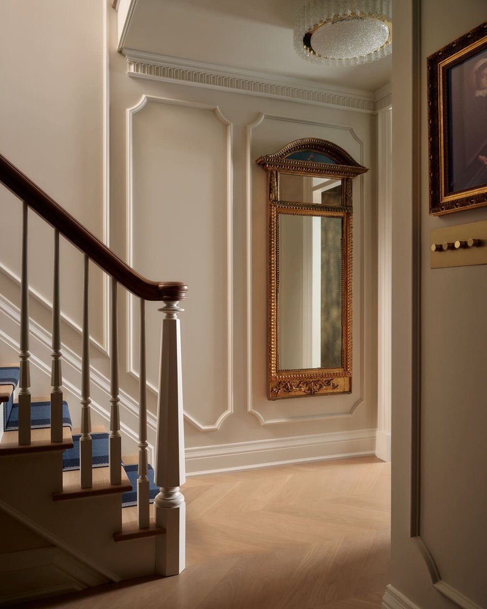 Elegant staircase landing with paneled walls, blue carpet runner, and ornate gold mirror in a Toronto home