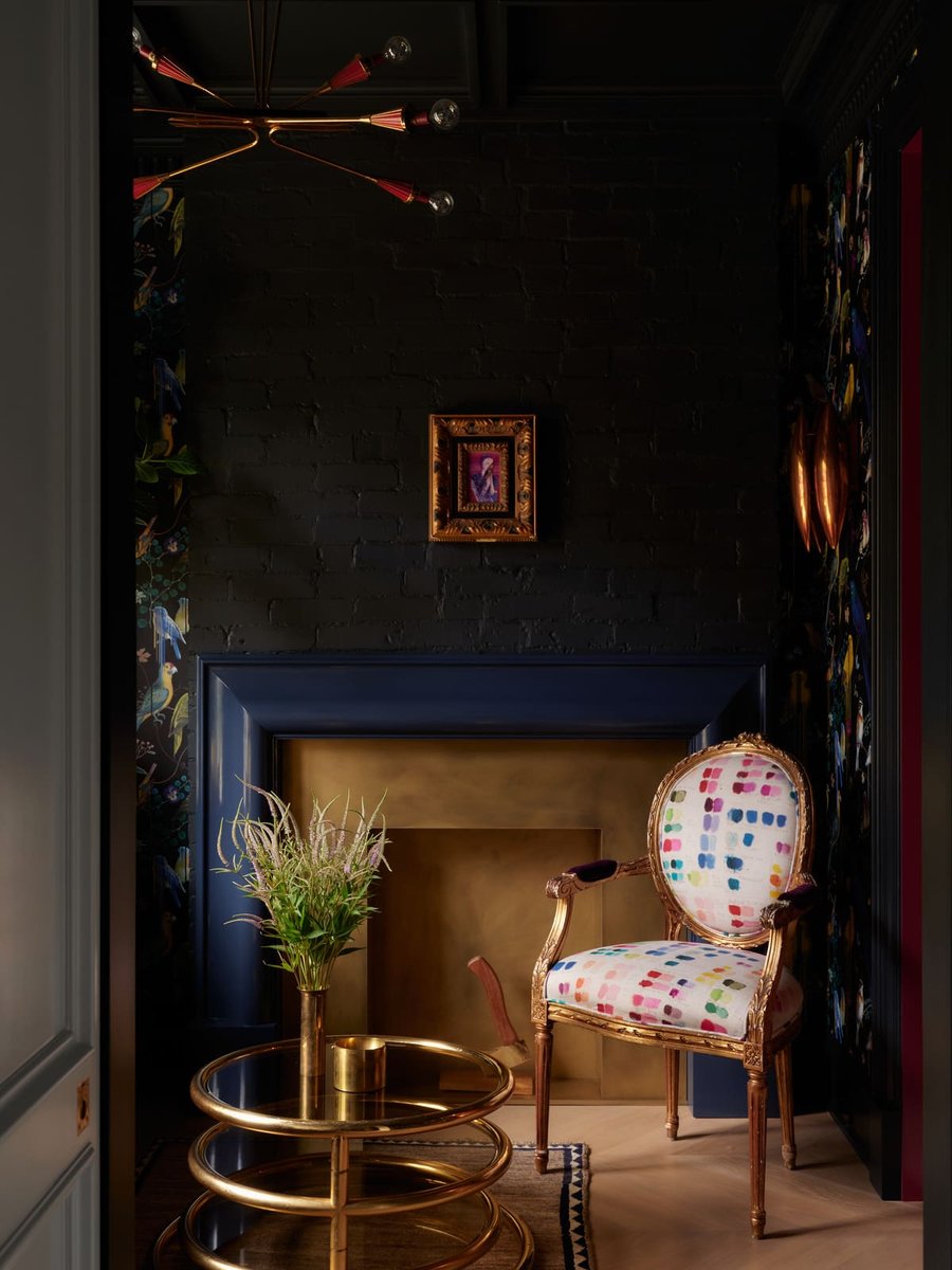 Moody Toronto sitting nook with black brick walls, gold accents, patterned chair, and round brass table under sculptural lighting