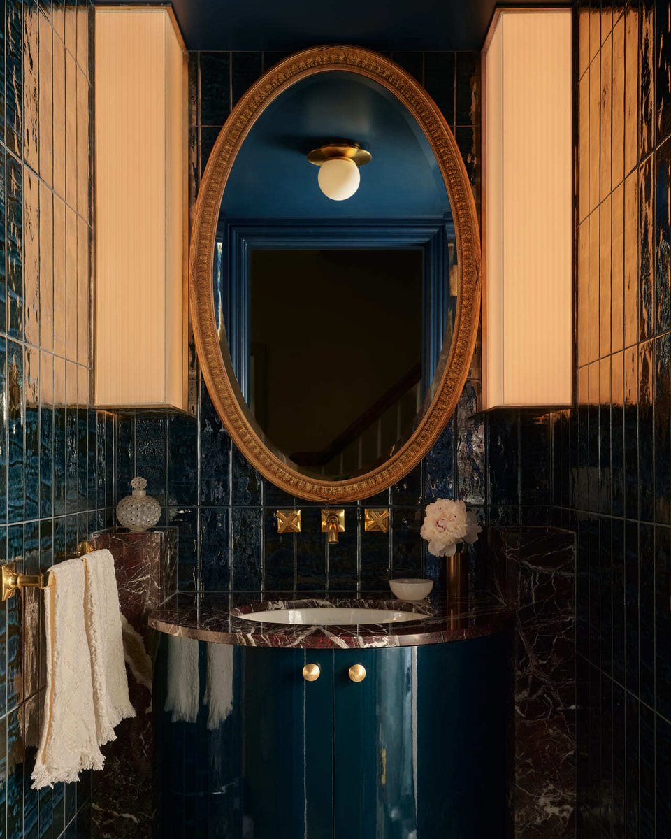 Moody powder room with oval mirror, blue tile walls, brass fixtures, and marble vanity in Toronto