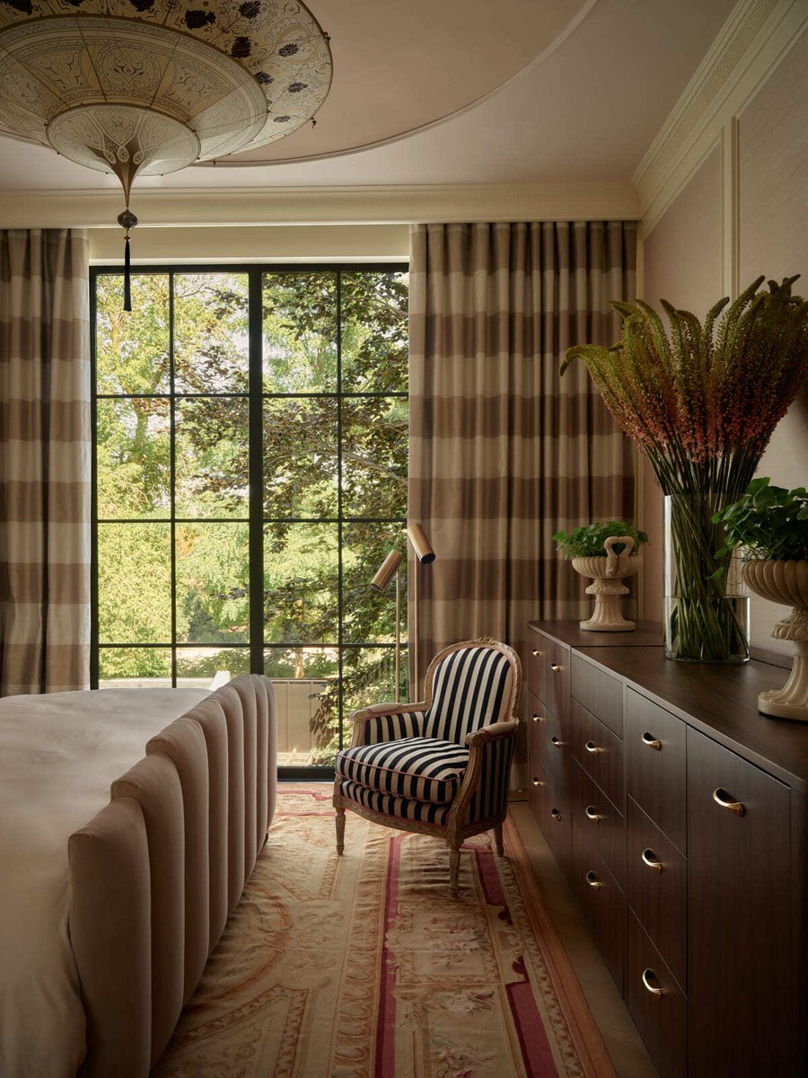 Toronto bedroom with upholstered bed, striped armchair, large window, patterned rug, and soft neutral tones with classic details