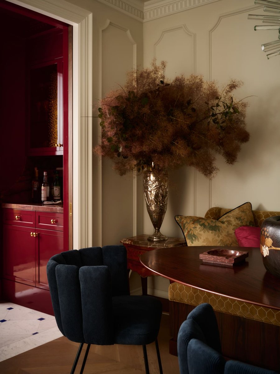 Toronto dining area with dark wood table, blue velvet chairs, floral arrangement, and red bar cabinetry in an elegant interior