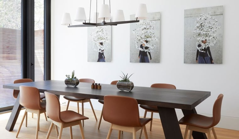 Dining Area in Home With Hanging Light Pendant and Large Table With Eight Chairs and Three Art Pieces on Wall