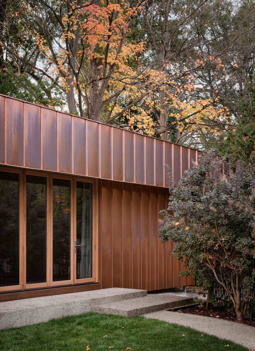 Toronto contemporary home with weathered copper siding, floor-to-ceiling windows, and autumn trees creating a warm natural backdrop