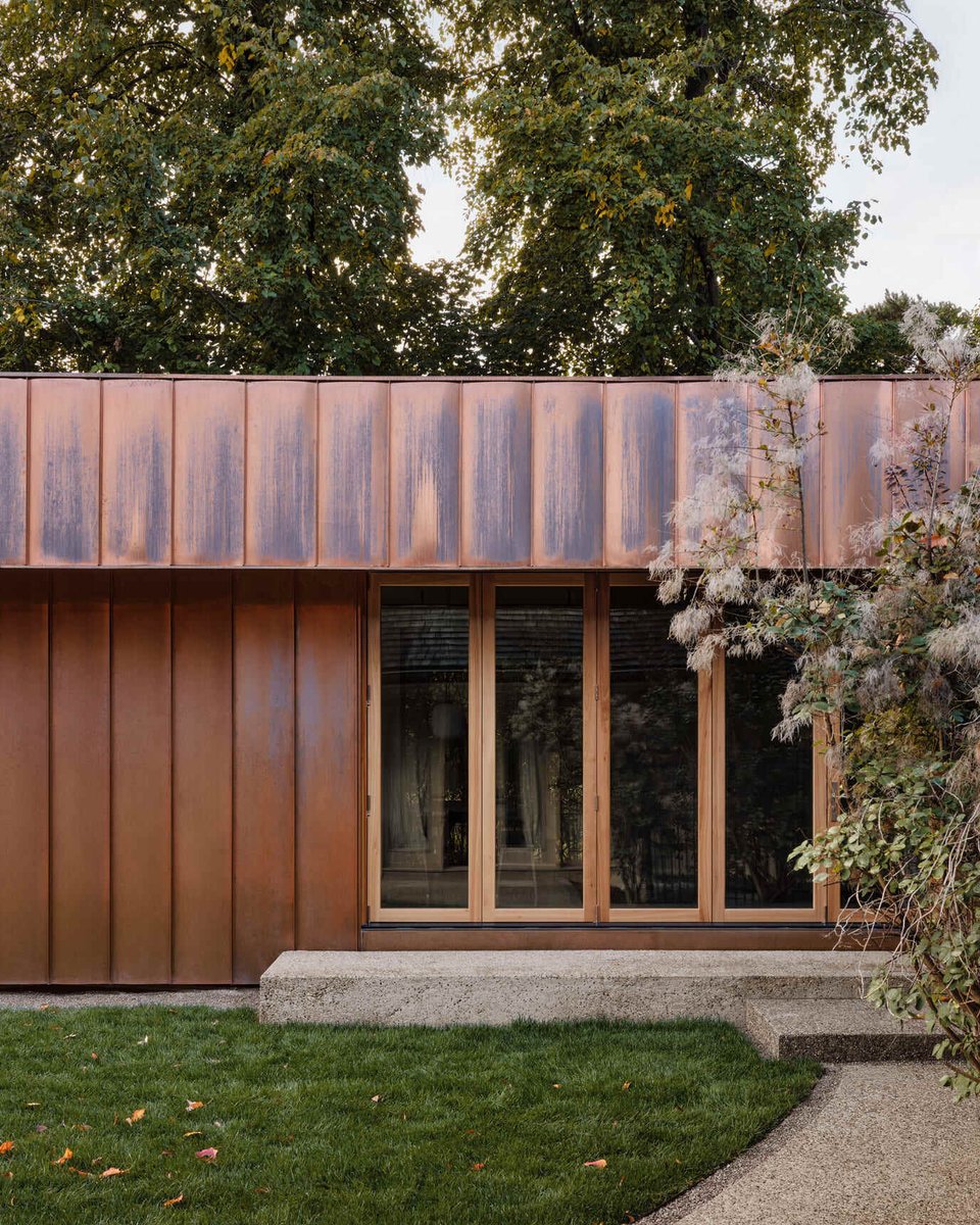 Toronto copper home exterior detail with patina panels, wood-framed glass doors, and garden greenery blending modern design with nature