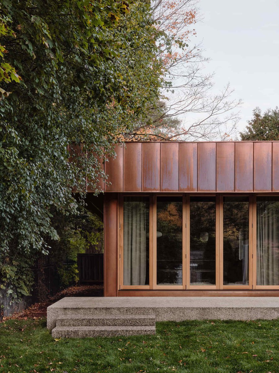 Toronto copper-clad home exterior with large glass doors, concrete steps, and lush trees framing a modern backyard addition