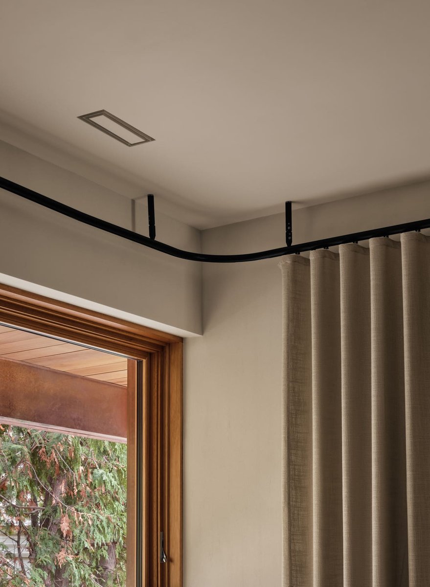 Toronto interior detail of curved black curtain track and ceiling, with floor-to-ceiling drapes and wood-framed window