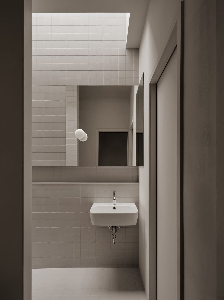 Toronto minimalist bathroom with white tile walls, wall-mounted sink, mirror, and skylight bringing in soft natural light