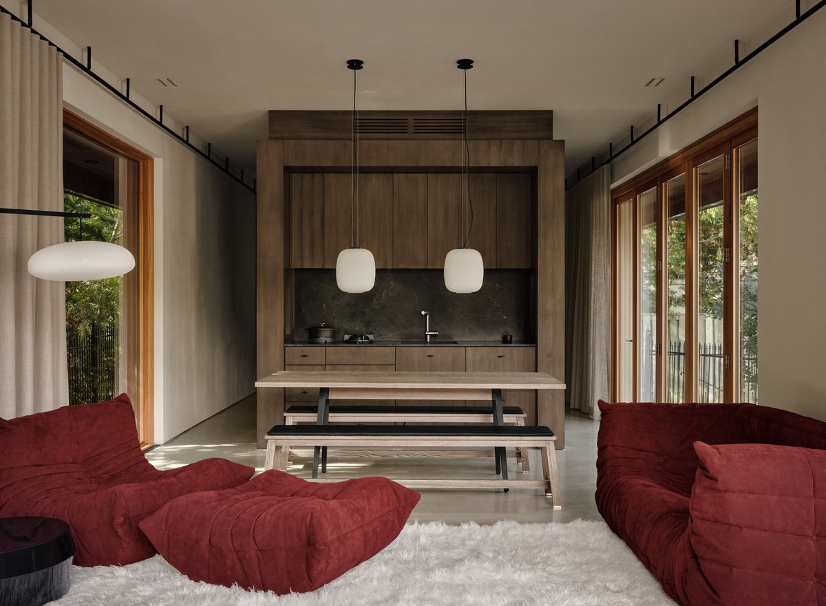 Toronto modern interior with wood kitchen, pendant lighting, long dining table, and red lounge seating in a minimalist open-concept space