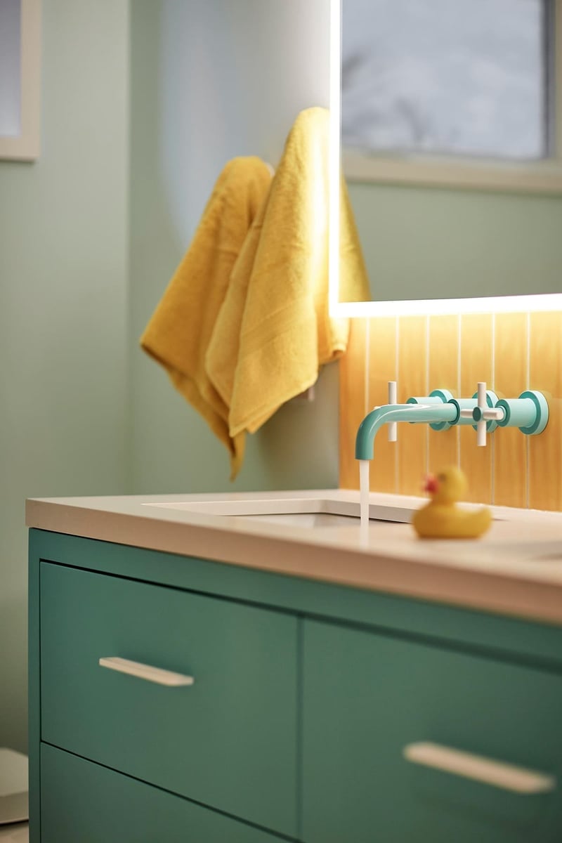 Kids bathroom sink with blue faucet and cabinets with yellow backsplash behind