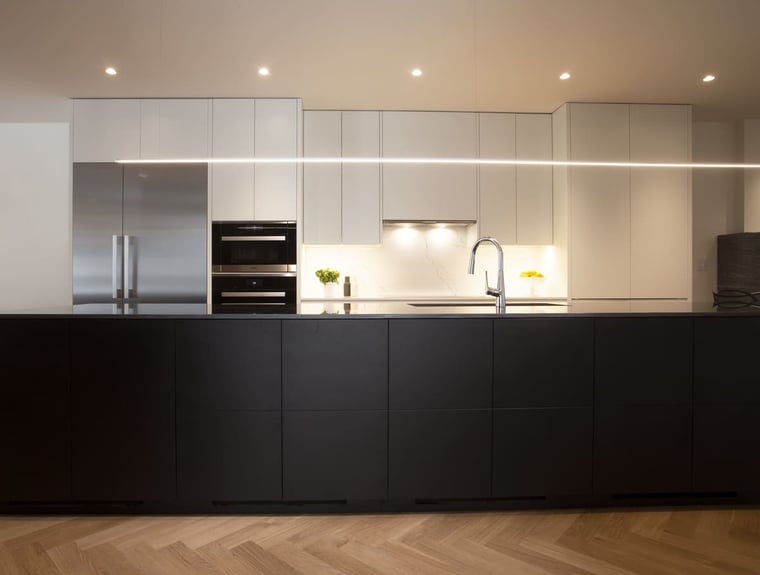 Large kitchen island with black flat panel cabinets below minimalist style light fixture in Toronto