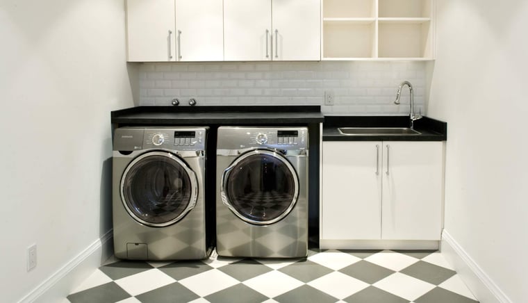 Modern laundry room in Toronto with black countertop, white cabinets, and Samsung front-load washer and dryer