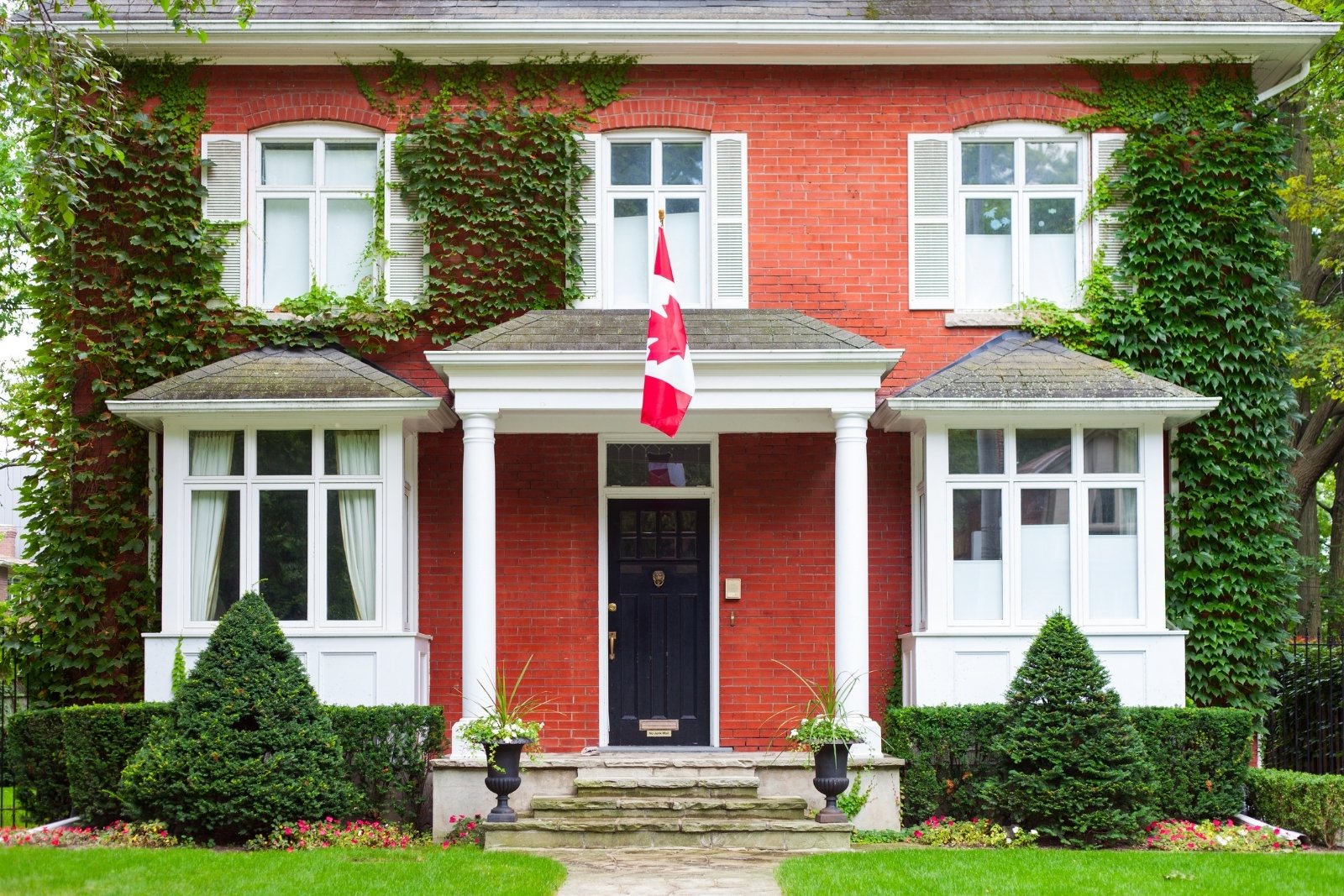 Red brick Toronto home with white trim, lush greenery, and Canadian flag Severnwoods