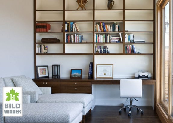 Toronto home office with built-in wood shelving, desk workspace, books, chaise lounge, and large window bringing in natural light