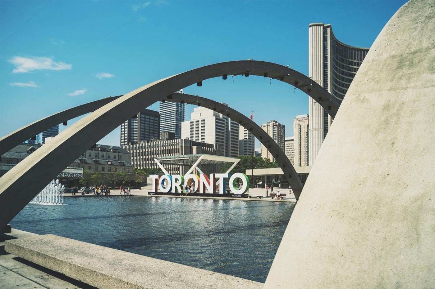 Toronto’s iconic city sign at Nathan Phillips Square, framed by concrete arches and surrounded by modern high-rise buildings