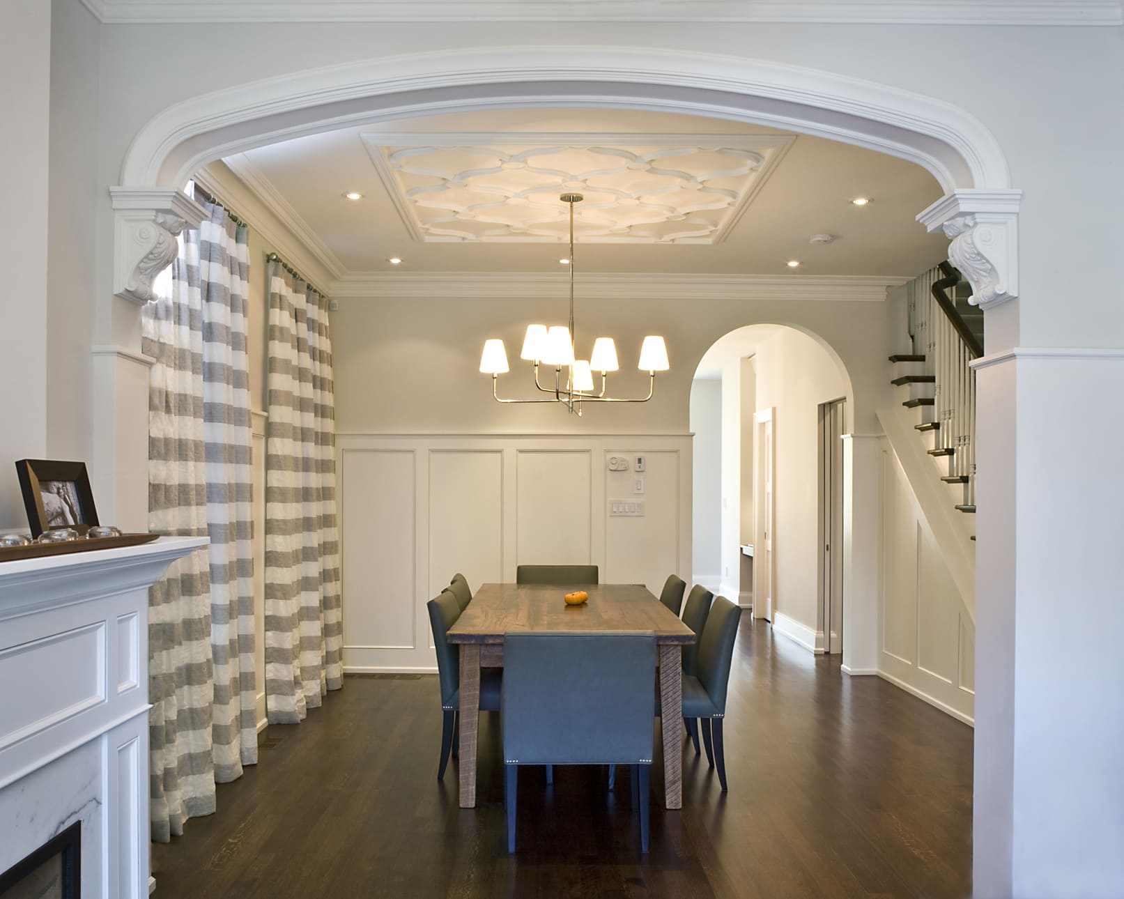 Dining Room Area With Rectangular Table and Chairs in Center. Chandelier Hanging Light Fixture Drops from Ceiling Above With Archway