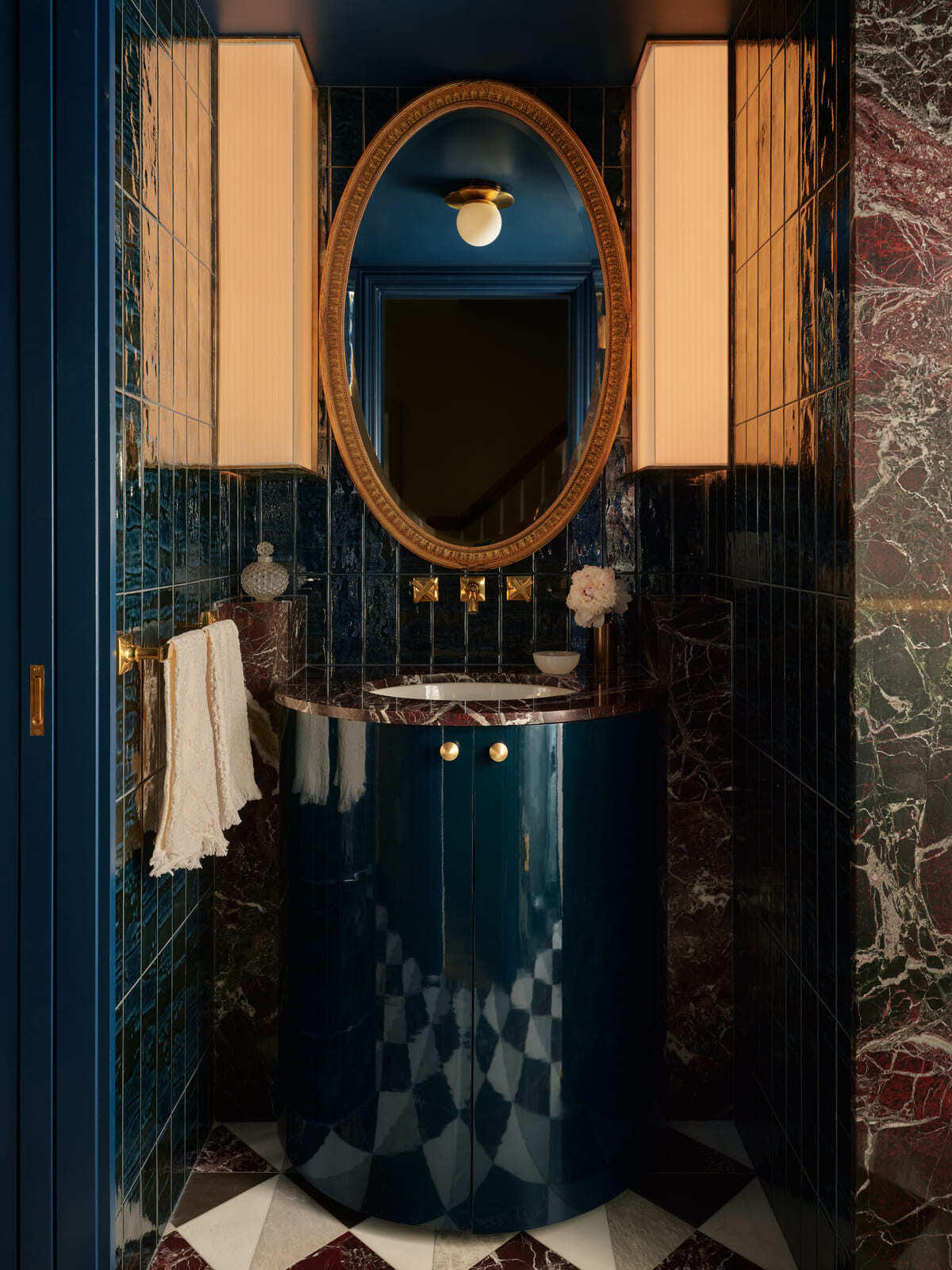 Elegant powder room featuring blue cabinetry, oval mirror, marble countertop, and warm lighting in Toronto