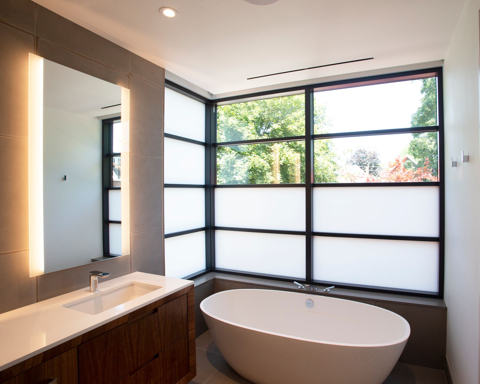 Modern bathroom with soaker tub by window and backlit mirror