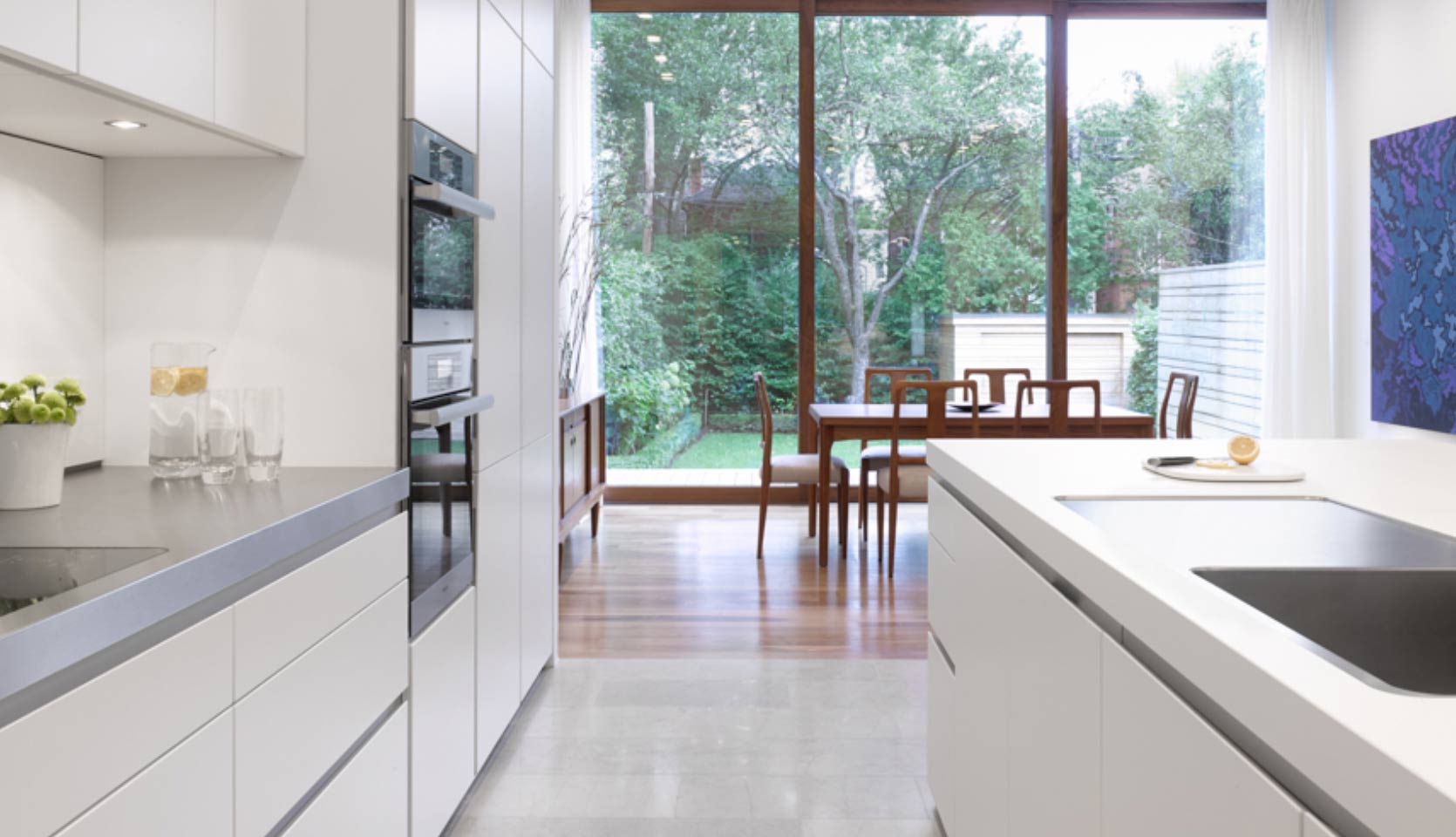 View of Kitchen and Dining Area with White Flat Panel Cabinets and Large Floor to Ceiling Windows